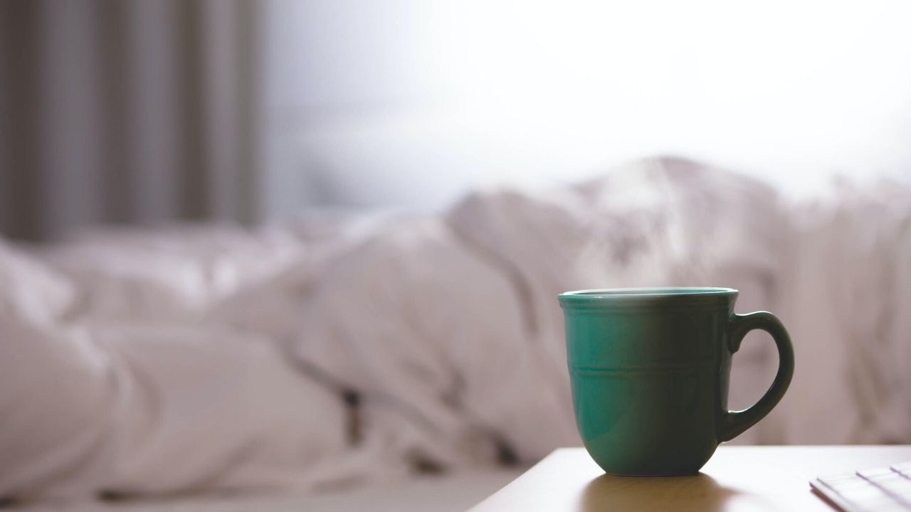 featured photo of a cup of coffee by a bed which helps with new mom sleep deprivation