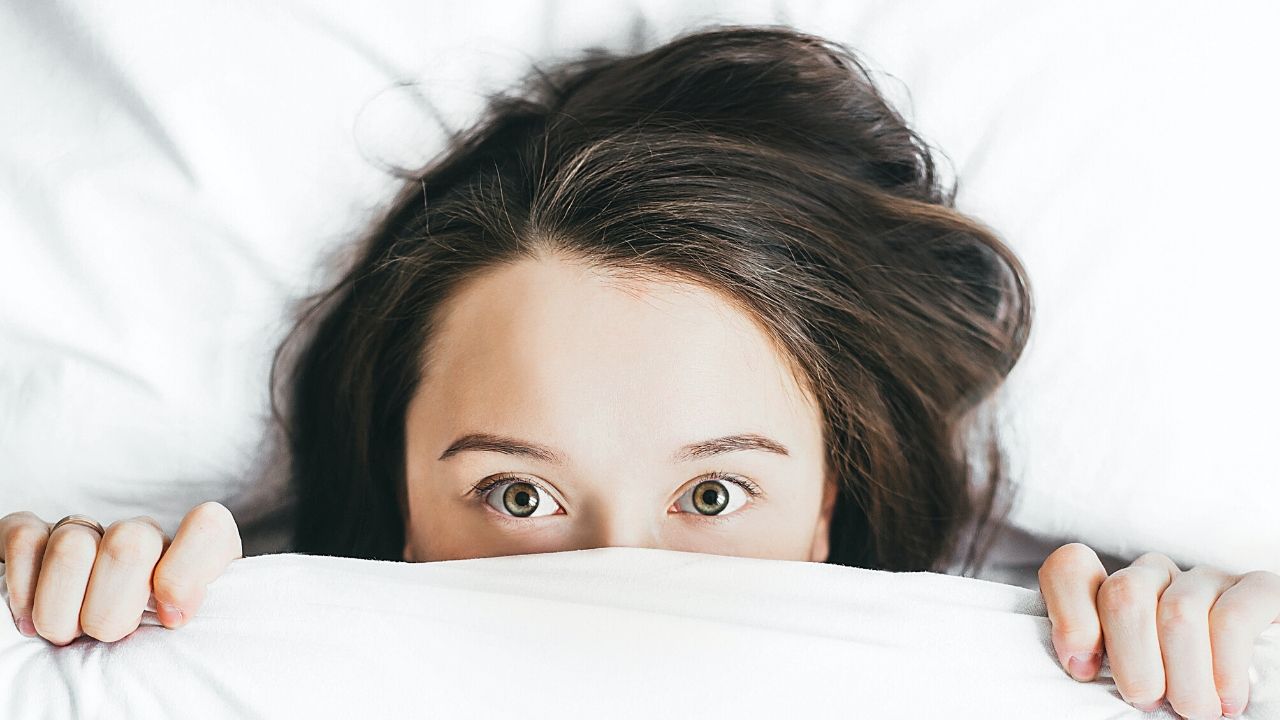 photo of a woman peeking out from under a blanket