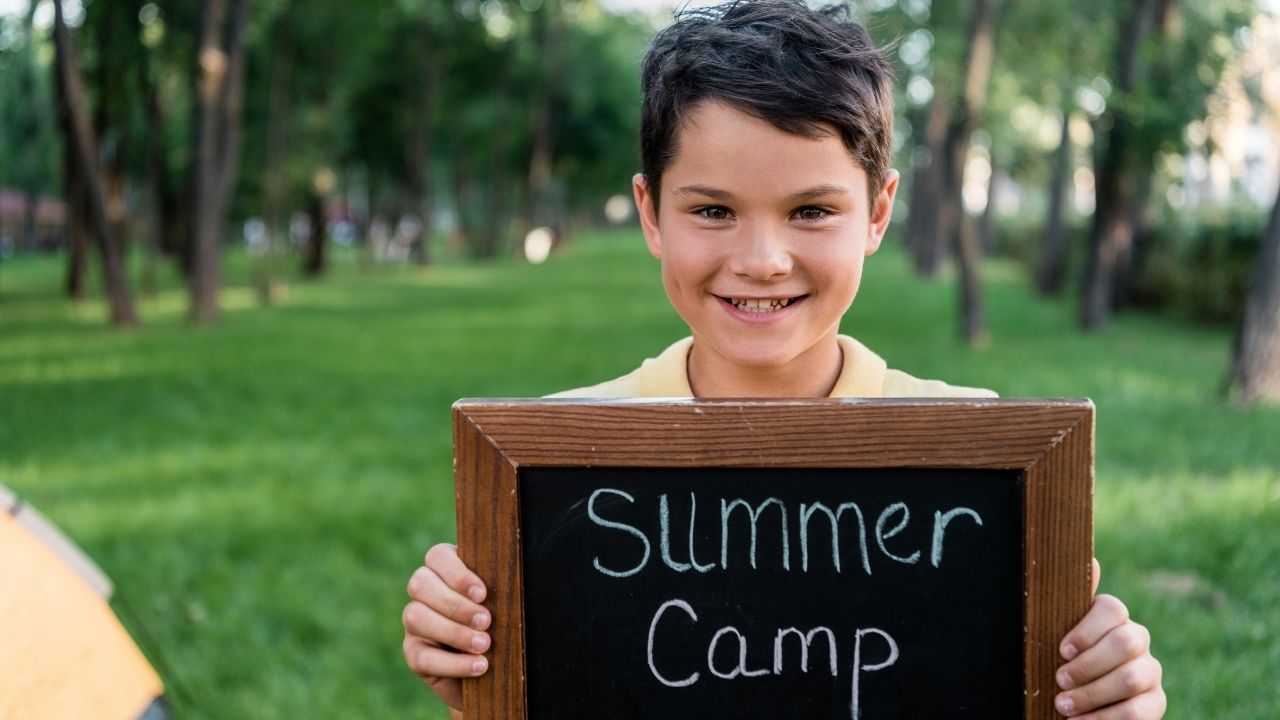 boy holding a sign - the featured image for the article on at home summer camp themes