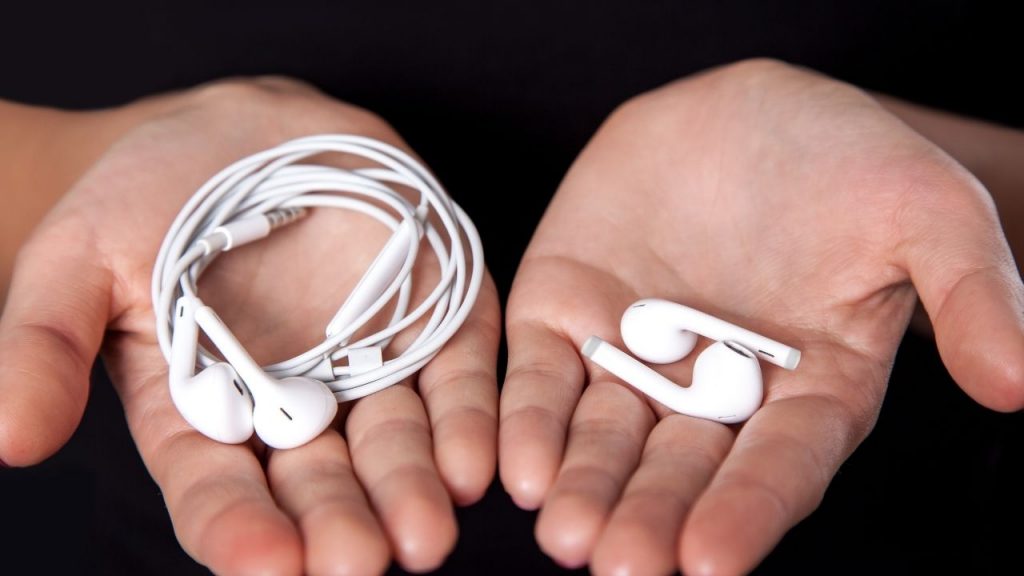 photo of hands holding wire earbuds and wireless earbuds