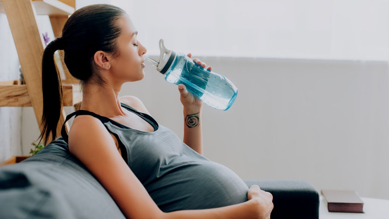 pregnant woman drinking from a blue water bottle