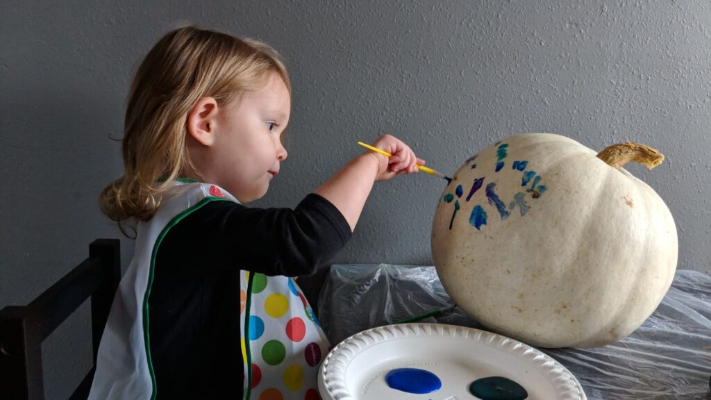 my toddler painting a white pumpkin as a fun way to celebrate halloween with kids